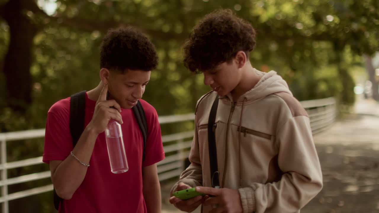 Teenage friends talking and looking at a smartphone outdoors