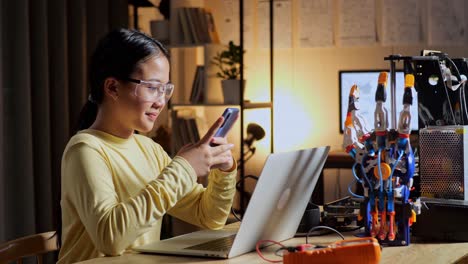 teen asian girl using smartphone while working about a cyborg hand on a laptop at home