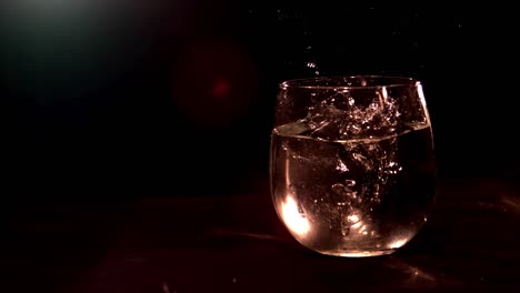 Dunkle-Filmische-Szene-Von-Eis-In-Superzeitlupe,-Das-In-Ein-Glas-Wasser-Fällt,-Aufgenommen-Mit-5000-Fps-Auf-Einem-Phantom-Flex