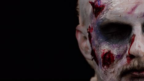 frightening man face with halloween zombie bloody wounded makeup, trying to scare, face expressions