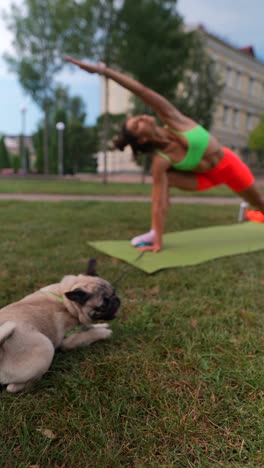 woman practicing yoga in a park with a puppy