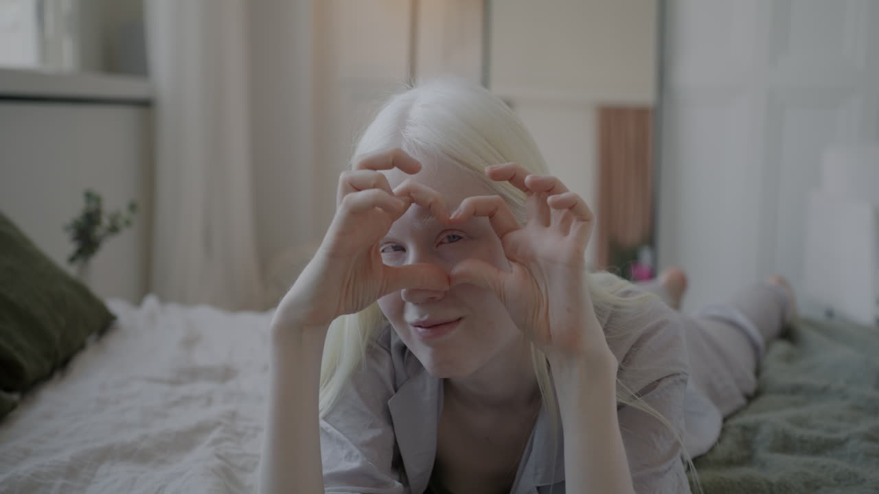 Woman lying on bed making heart shape with hands