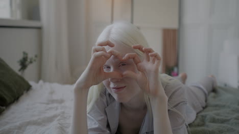 woman lying on bed making heart shape with hands