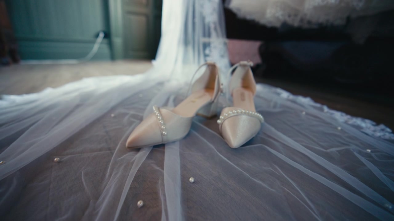 Elegant bridal shoes rest on a sheer veil in soft indoor light, capturing delicate fabric, quiet anticipation, and the refined atmosphere of wedding preparation before the ceremony.