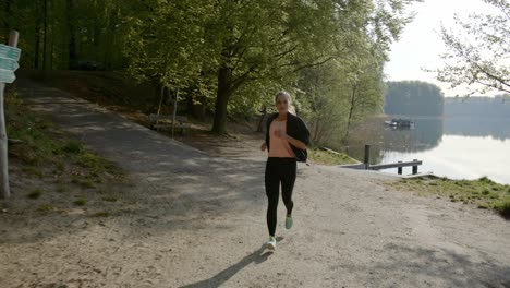 Woman-running-past-lake-and-woods-on-sunny-day