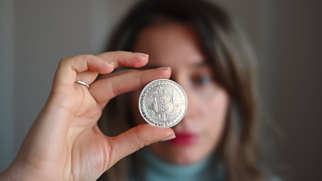 Donna mora con una camicia blu che tiene in mano un bitcoin argentato
