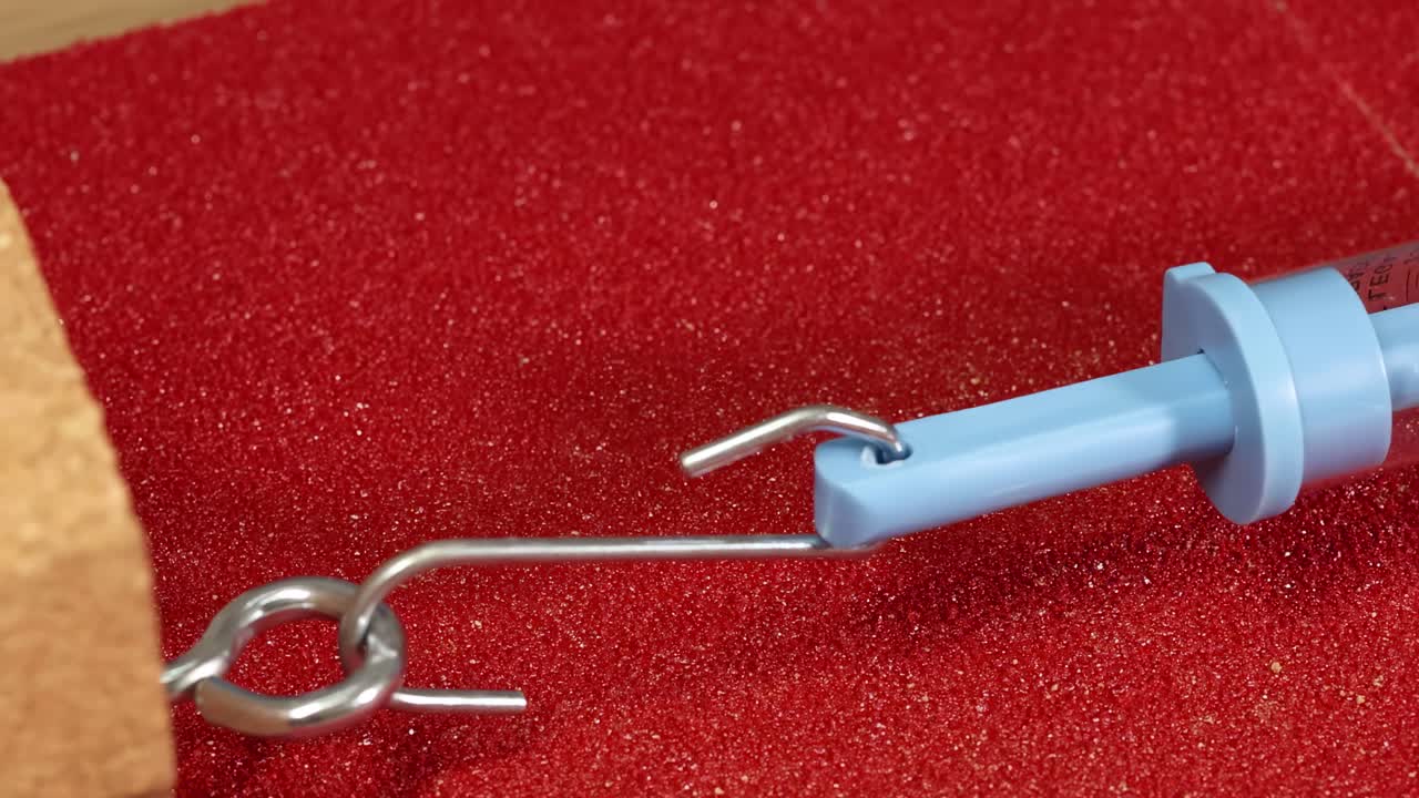 A spring scale hook is manipulated on a textured red surface with a wooden block.