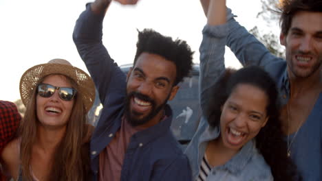 excited friends on a road trip cheering beside camper van