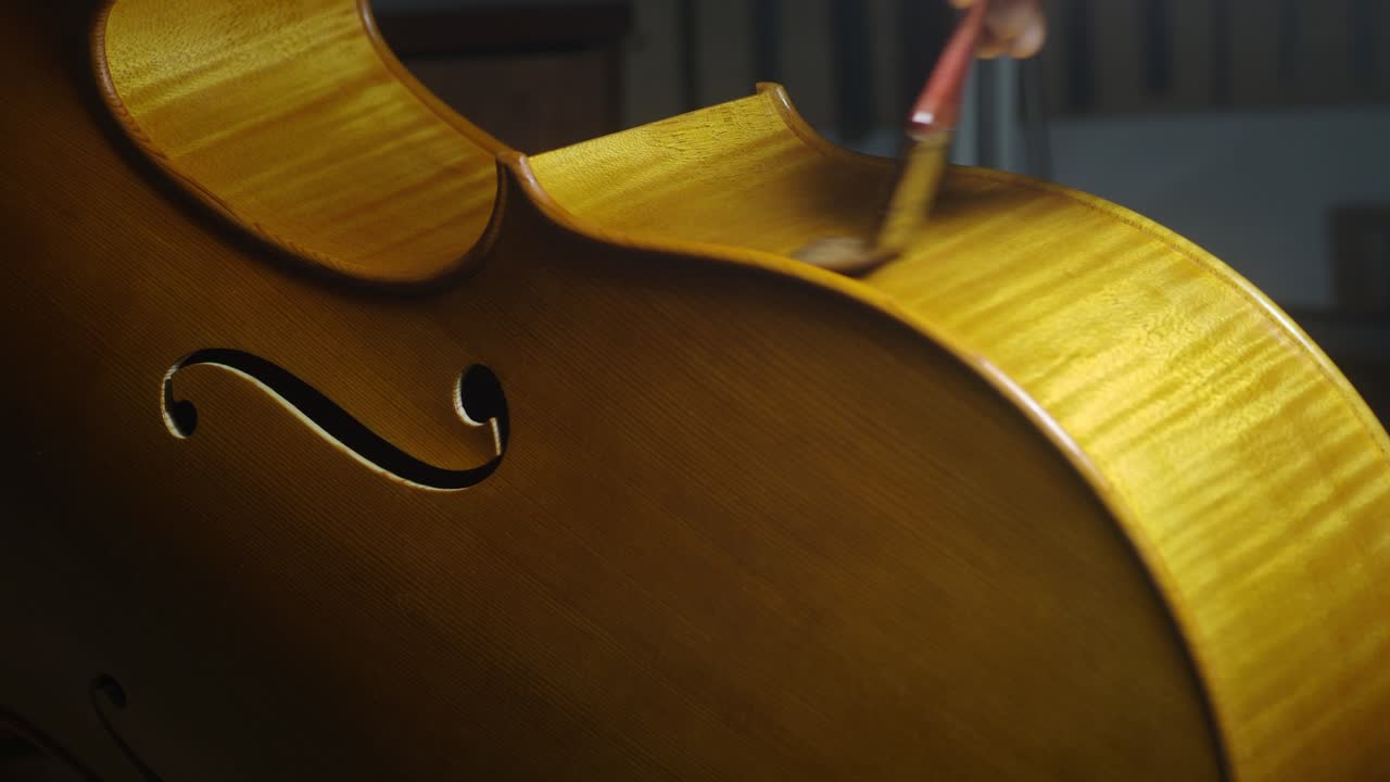 Luthier carefully varnishing cello ribs with self produced varnish, showcasing the craftsmanship and precision involved in creating high quality musical instruments in a specialized workshop