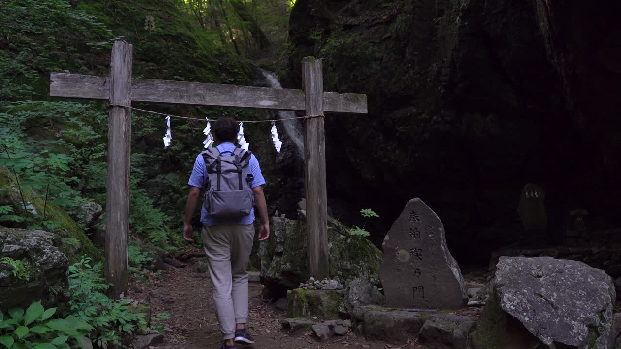 excursionista masculino caminando a través de una pequeña puerta torii japonesa en el bosque - plano medio