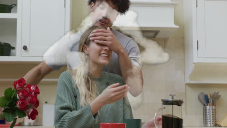 Animation-of-cloud-house-over-happy-diverse-husband-giving-wife-with-flowers-in-kitchen