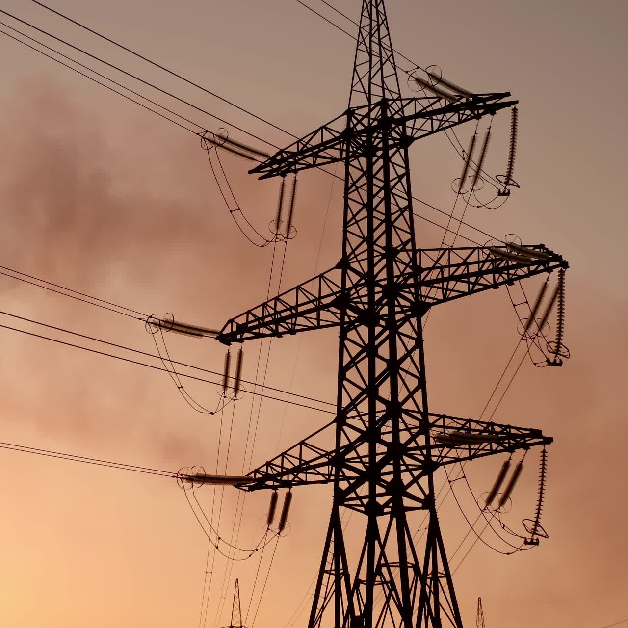 High voltage electric lines and industry. Pipes with dark smoke near the transmission electric towers at dusk. Pollution the atmosphere. View from below