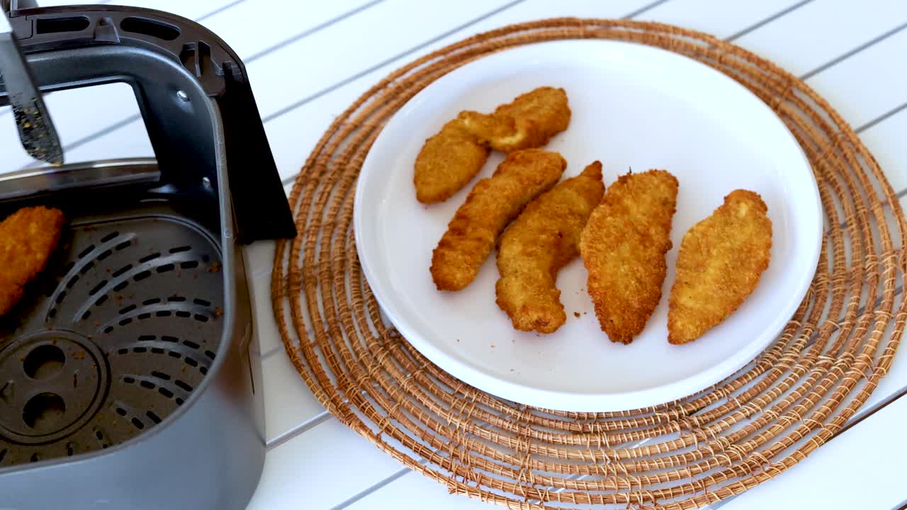 Golden chicken pieces transferred from air fryer to plate using tongs. Bright kitchen setting with natural lighting