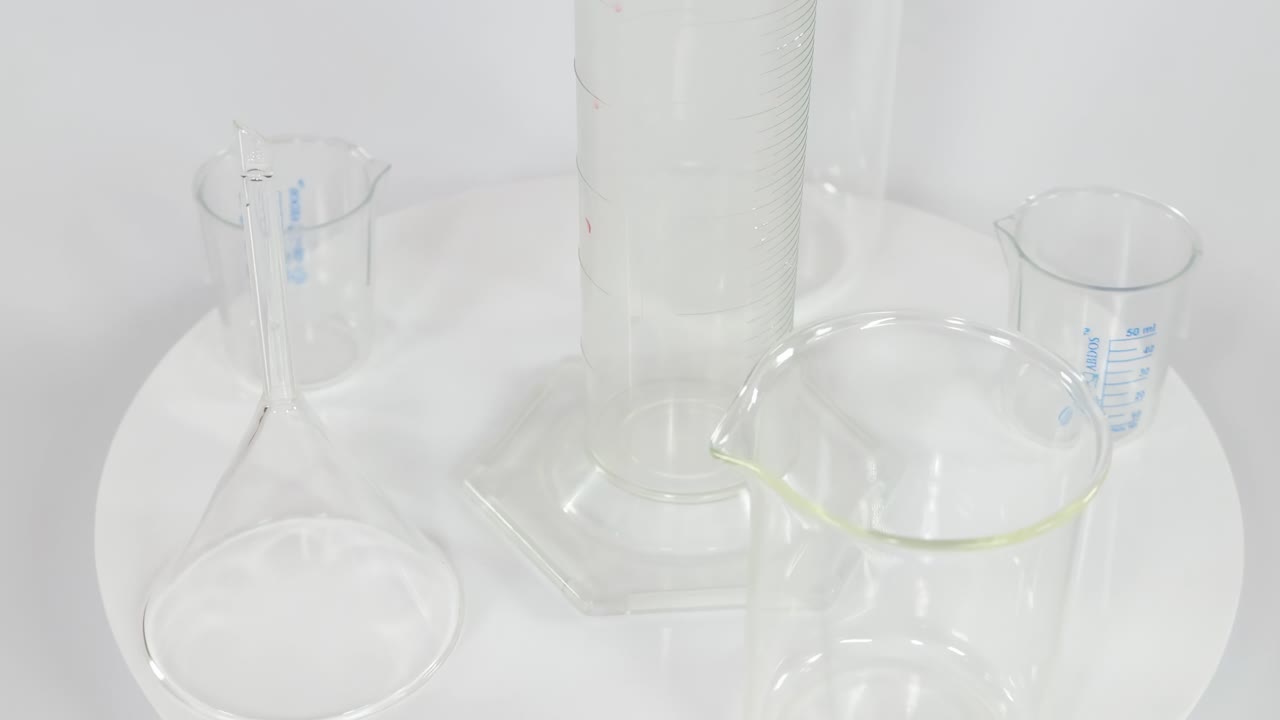 A variety of clear laboratory glassware, including beakers and cylinders, arranged on a rotating white platform.