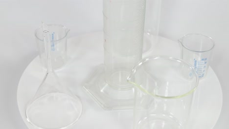 a variety of clear laboratory glassware, including beakers and cylinders, arranged on a rotating white platform.