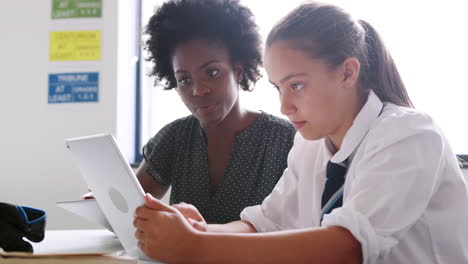 tutora de escuela secundaria con tableta digital dando a una estudiante que lleva uniforme una a una enseñanza en el escritorio