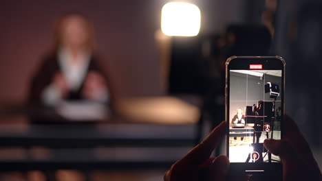 footage on smartphone in photo studio. close up. woman sits at desk in blurred backdrop. blogging concept.