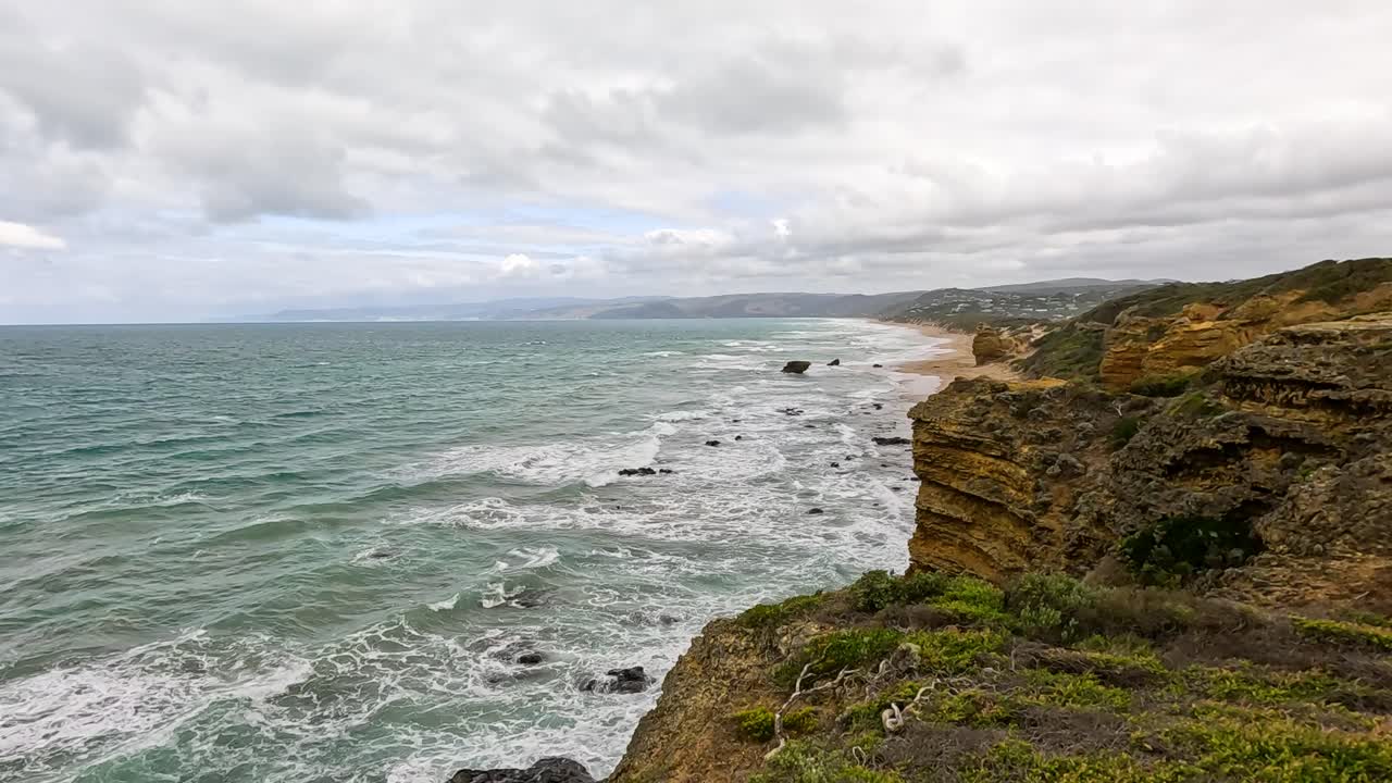 Aerial footage captures rugged cliffs and ocean waves under overcast skies along Australia's Great Ocean Road