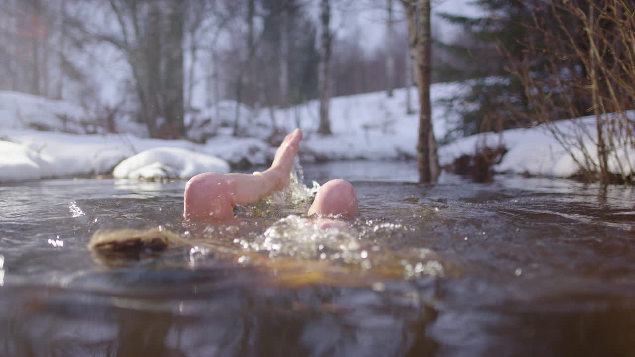 Woman takes dip in river through snowy woods after sauna, Scandinavian lifestyle