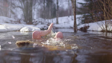 woman takes dip in river through snowy woods after sauna, scandinavian lifestyle
