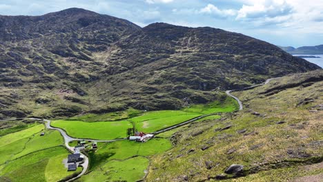 drone volando a un paso de carretera en las montañas con el paso de carretera granja en campos verdes exuberantes, west cork irlanda
