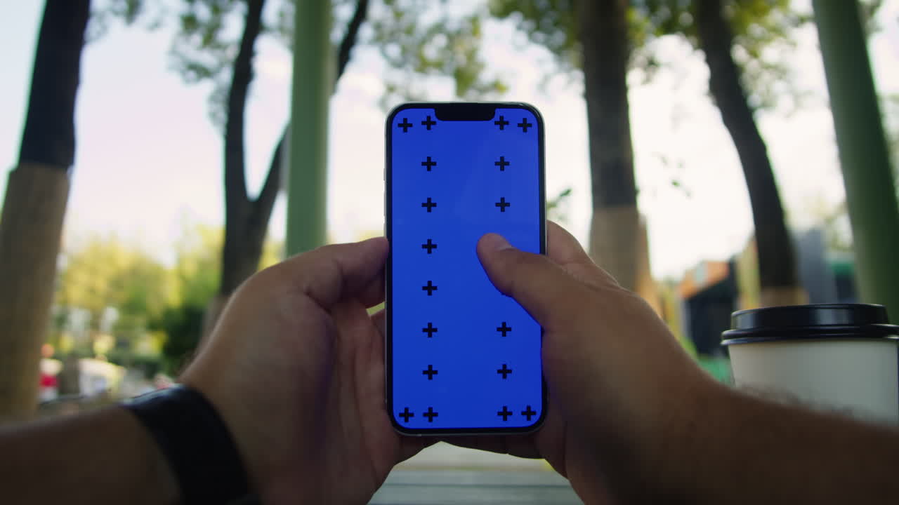 Young woman holding and swiping phone chroma key screen in the park in front of trees close-up. Girl with green screen on smart phone. Nature