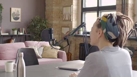 Young-Man-Sitting-At-A-Table-With-Microphones-And-Computer-To-Record-A-Podcast-With-A-Woman