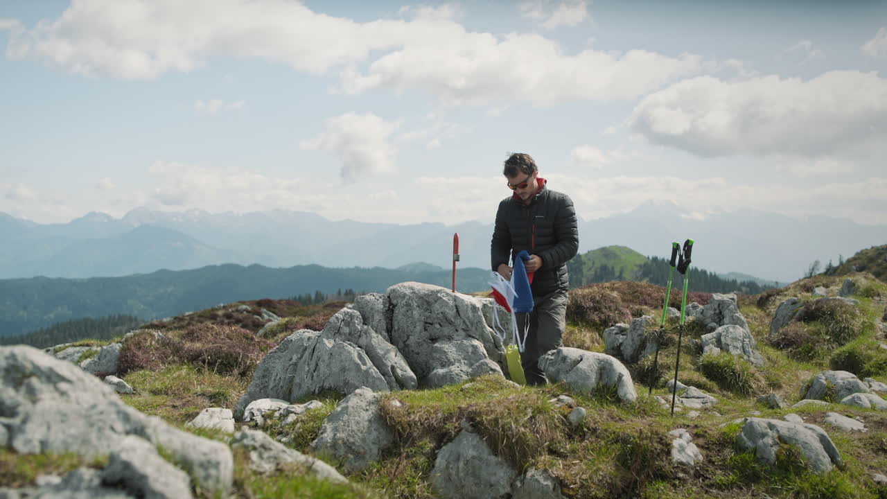 excursionista sacando una bandera eslovena de su mochila y extendiéndola sobre una roca