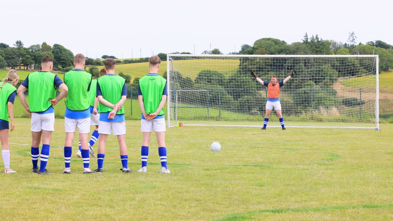 Male and female soccer players playing soccer, one player shooting at goal and goalkeeper on pitch