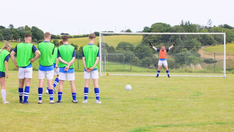 male and female soccer players playing soccer, one player shooting at goal and goalkeeper on pitch