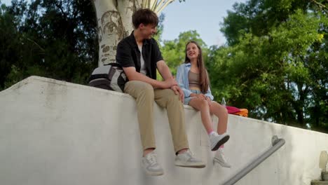 young couple sitting on a wall in a park, talking and smiling