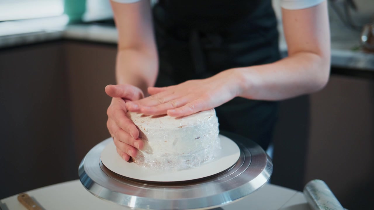 Baker carefully rotates a cake on a stand. Hands gently smooth frosting with precision and care. Scene shows focus, calmness, and skill in cake decorating. Perfect for food blogs, culinary tutorials
