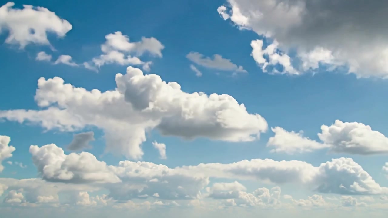 Stirring wind pushing cumulus clouds drifting right and upward over low horizon, revealing blue sky