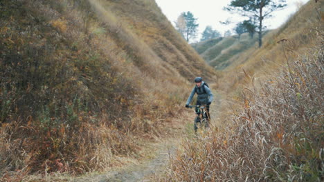 ciclista masculino con mochila y casco montando una bicicleta de montaña en la colina por la carretera en medio del valle