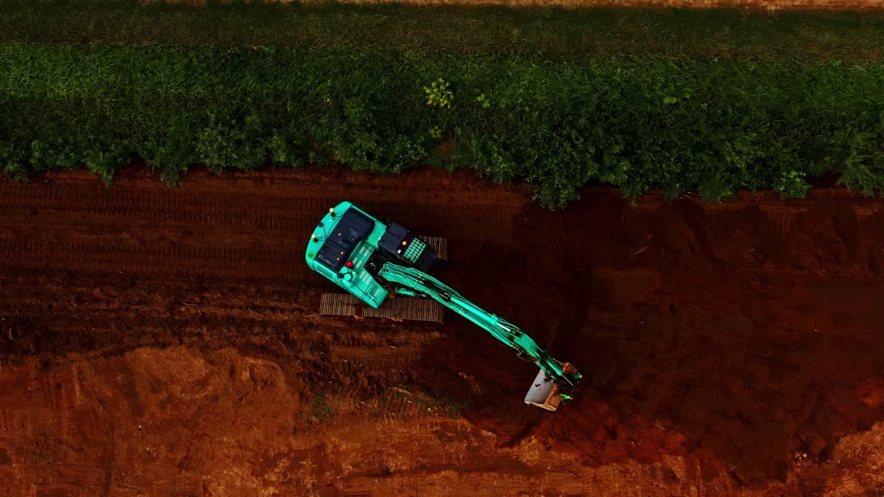 Aerial top down of Excavator Digging Rich Red Soil During Earthworks on Industrial site