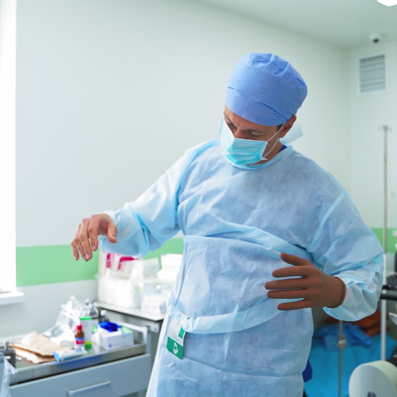 Modern surgery room. Assistants help the doctor to dress medical uniform and sterile gloves before the operation. Health care concept.