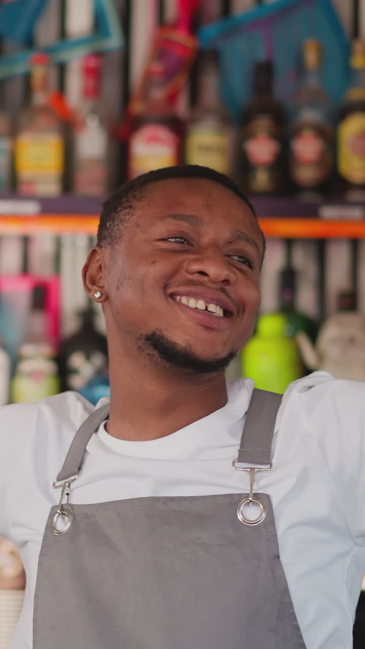 jovem barman dança na bancada do bar. o barman afro-americano mostra um gesto de paz desfrutando da atmosfera de festa. o garçom preto se diverte contra a prateleira com garrafas