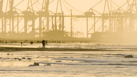 Silhouette-of-industrial-container-harbor-with-sandy-beach-and-people-in-foreground