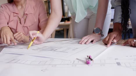 midsection of diverse female architects discussing blueprints at desk in office, in slow motion