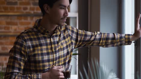 mixed race man drinking coffee and looking over the window