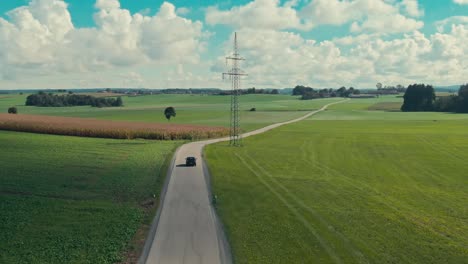 car driving on a country road amid green fields, sunny day, aerial shot