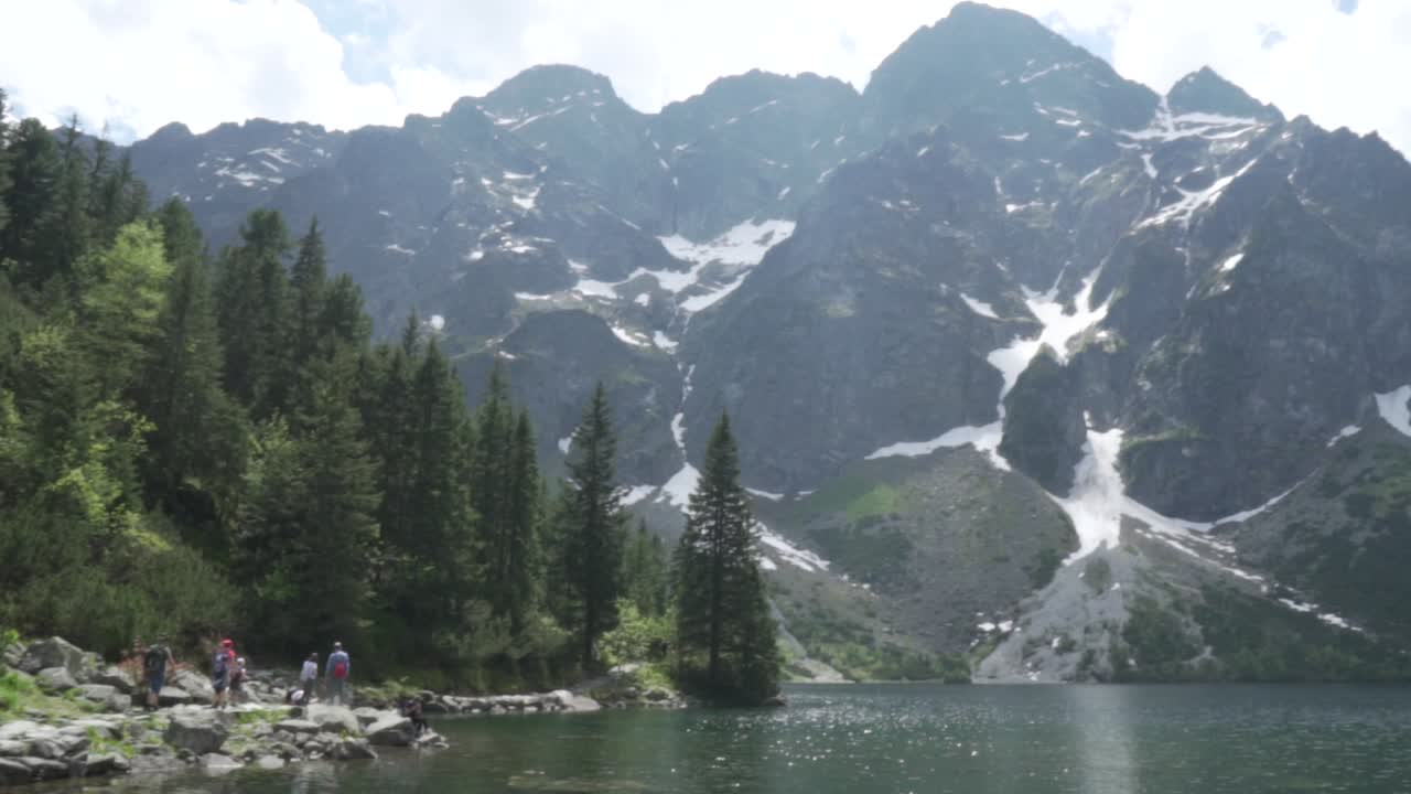 Pan shot of the lake of Morskie Oko with tourists walking on a summer day.