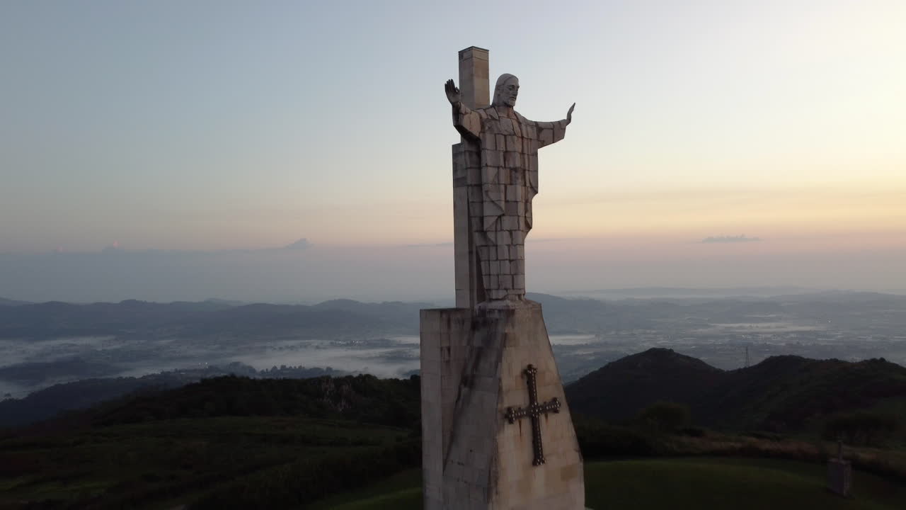 drone volando en la cima de una montaña, al lado de una gran estatua de hormigón de jesús