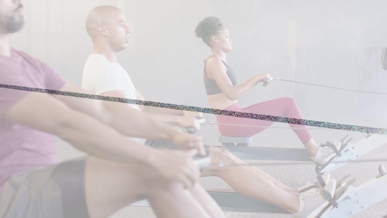 Middle man initiating drive while trio doing in-sync strokes on rowing machines for fitness class