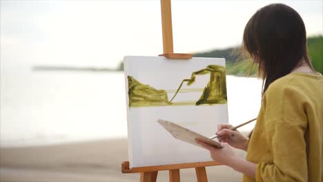 mujer pintando un paisaje marítimo en la playa