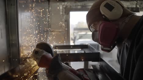 worker wearing protective gear grinds metal shelves with power tool, sparks fly- slow mo