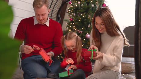 happy family wrapping christmas presents sitting on the floor near a christmas tree in living room