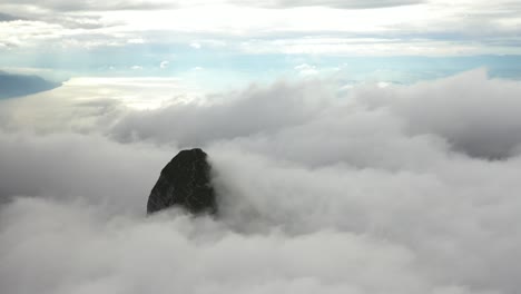 drone shot of a mountain top barely peeking through the clouds that are moving fast, passing by