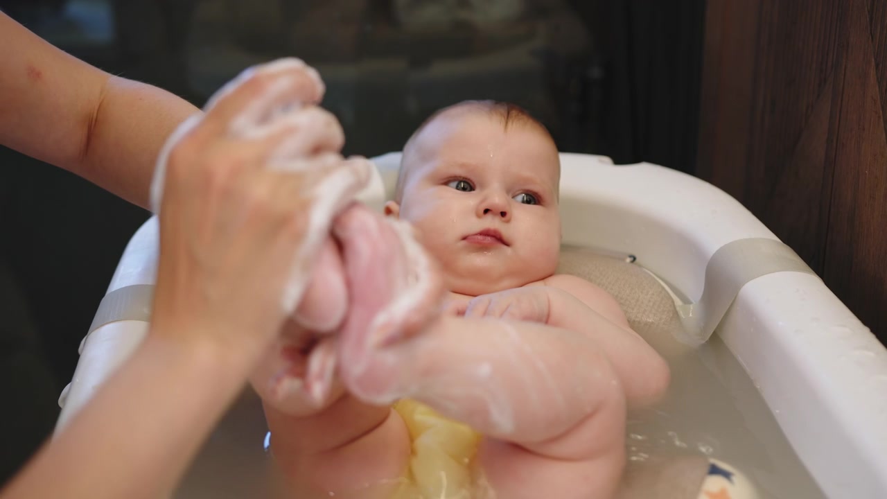 Un progenitor lava suavemente las manos y los pies del bebé con jabón y agua en una bañera, creando un ambiente limpio y.
