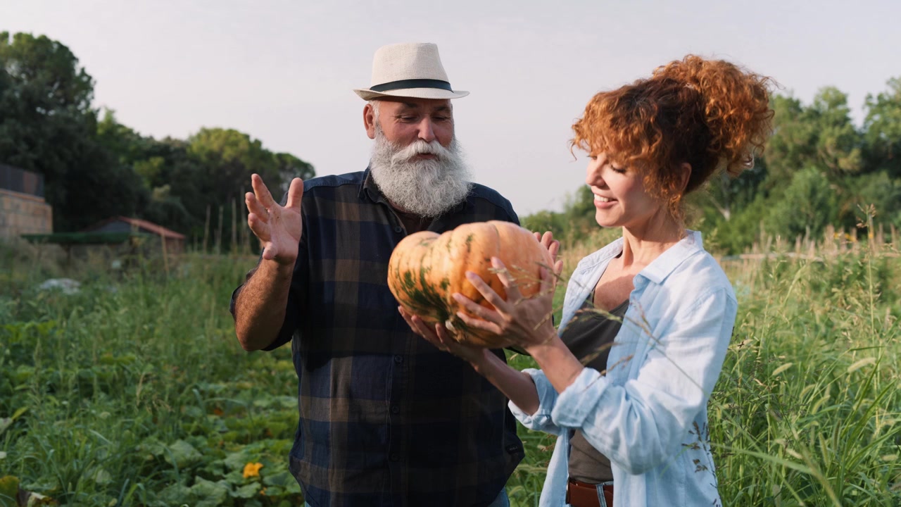 Starší farmář a mladá žena drží dýni v zeleninové zahradě.